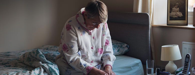 Elderly woman sitting alone on her bed