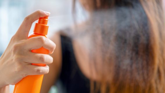 Young woman applying hair spray in bathroom
