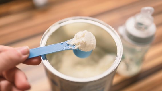 hand holding a scoop of baby formula powder from can