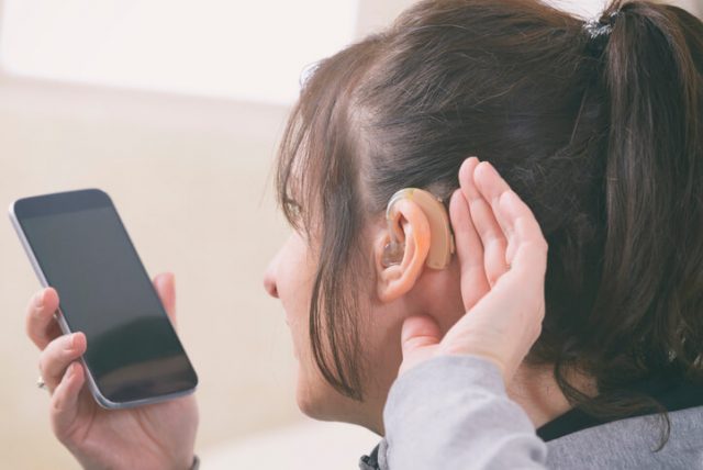 Deaf woman wearing hearing aid and using smartphone